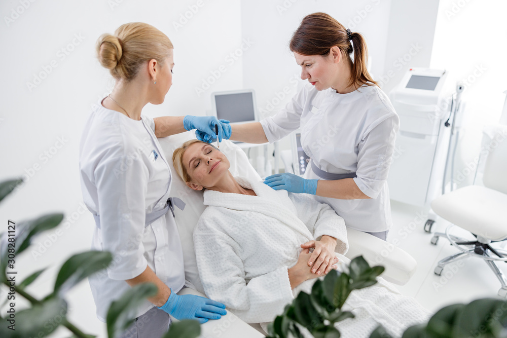 Obraz premium Specialists standing near smiling adult woman in beauty salon