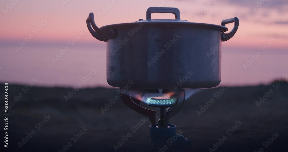 Boiling water using gas cooker outside near a Cliff with the sunset behing. Shot in Alentejo, Portugal