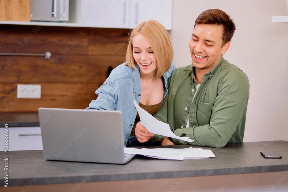 positive funny married couple checking their finance at home using laptop, discuss together, sit on table with papers positive funny married couple checking their finance at home using laptop, discuss together, sit on table with papers