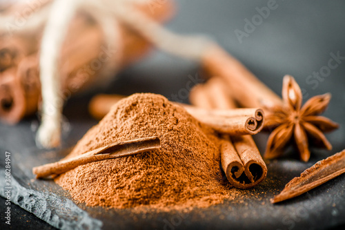 Fototapeta Naklejka Na Ścianę i Meble -  Heap of cinnamon powder on dark stone table. Cinnamons sticks in bunch at black board.