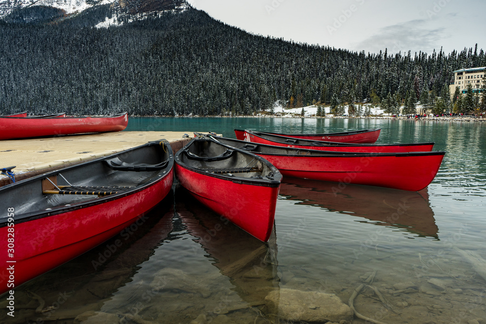 Red canoes sitting on a lake next to a dock with snow covered mountains in the background Red canoes sitting on a lake next to a dock with snow covered mountains in the background