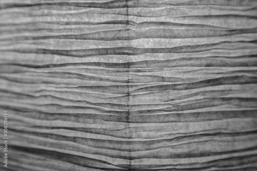 Fototapeta premium Close-up of a creased and backlit yellow paper lampshade in black and white. Focused on the center, blurred edges. High resolution full frame textured background.