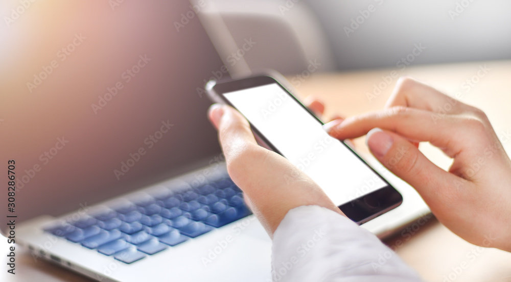 Girl pointing finger on blank screen cell phone wide banner, woman use cell phone, mockup white color background, Laptop computer blured keyboard.