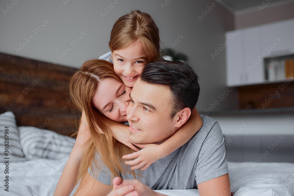 portrait of young caucasian family lying together on bed, young parents and child girl, happy together at home, spend free time at home on bed portrait of young caucasian family lying together on bed, young parents and child girl, happy together at home, spend free time at home on bed