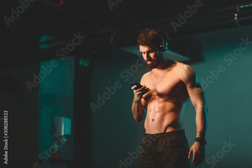 Shirtless young athletic man chooses music for workout in the gym © djile
