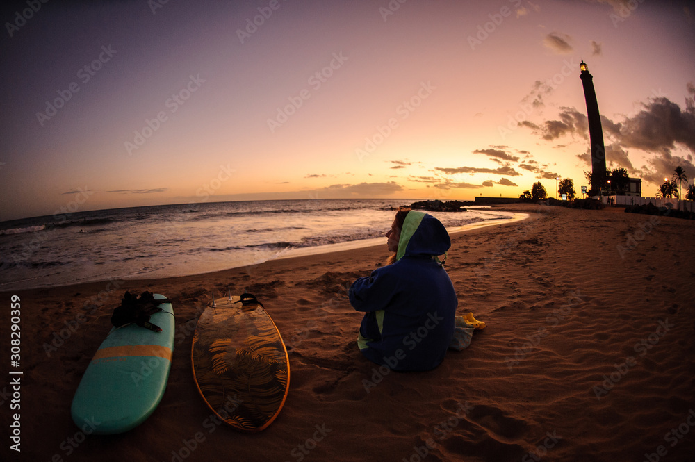 Φωτογραφία Fish-eye girl in the blue halaban sitting on the ocean shore near two surfing bo