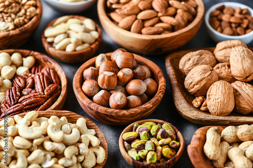 Mix of nuts in wooden bowls on dark stone table top view. Walnuts, cashew, almond, pistachio, pecan, hazelnut, macadamia nut. Healthy various super food selection.