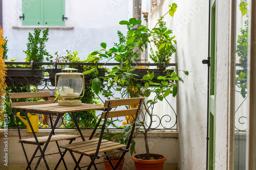 Billede på lærred An Italian balcony with green potted plants and garden furniture
