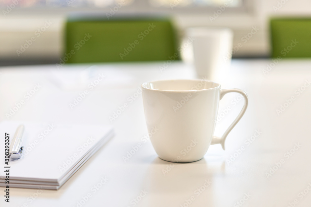 Weiße Tassen an einem weißen Tisch in einem Büro mit Blöcken, Stift und grünen Stühlen - selektiver Fokus mit sehr Tiefenunschärfe Weiße Tassen an einem weißen Tisch in einem Büro mit Blöcken, Stift und grünen Stühlen - selektiver Fokus mit sehr Tiefenunschärfe