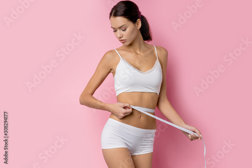 slim woman measuring her stomach using white measure tape after a diet isolated over pink background © alfa27
