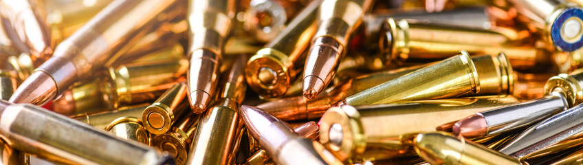 Pile of fire bullets or ammunition banner or panorama on dark stone table.  Hand guns weapon in background. Many projectiles into 9mm gun.