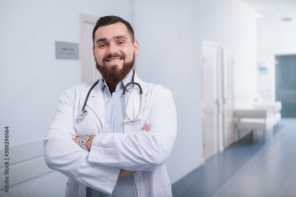Happy bearded doctor smiling to the camera, enjoying working in a modern hospital Happy bearded doctor smiling to the camera, enjoying working in a modern hospital