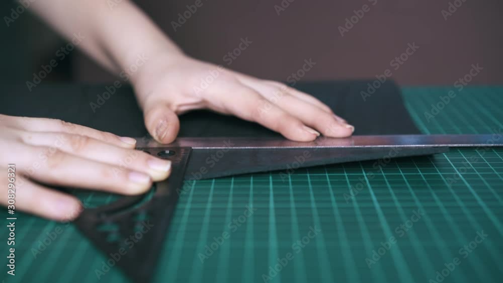 CU: Professional designer measures black leather cloth with metal and plastic rulers on cutting board close view CU: Professional designer measures black leather cloth with metal and plastic rulers on cutting board close view
