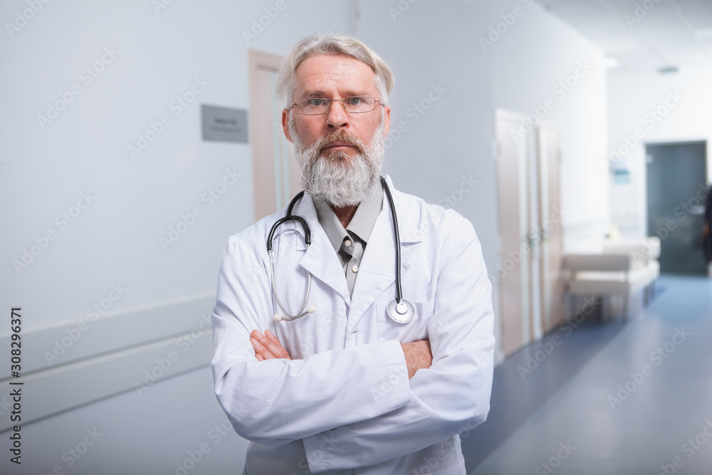 Experienced senior male doctor looking to the camera confidently. Serious elderly practitioner at the hospital Experienced senior male doctor looking to the camera confidently. Serious elderly practitioner at the hospital