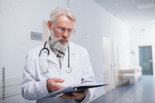 Professional medical worker reading documents on his clipboard, working at the hospital. Elderly doctor checking papers in the hallway of the clinic