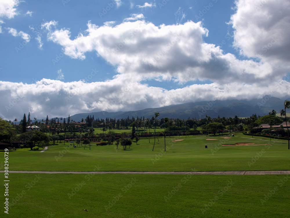 Green golf course in Hawaii with grey clouds and  a mountain in the background