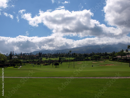 Green golf course in Hawaii with grey clouds and a mountain in the background