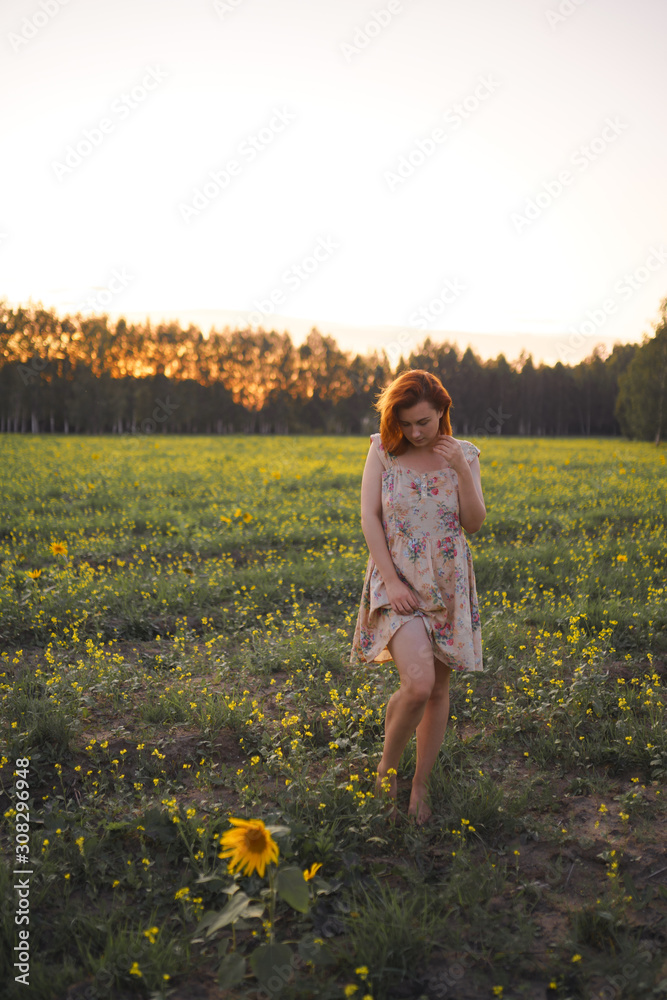 Fototapeta premium Beautiful redhead woman in a summer short dress during Golden Hour in a sunflower field in Eastern Europe Latvia Smarde