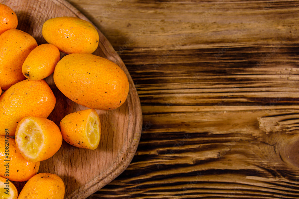 Cutting board with kumquat fruits on wooden table. Top view