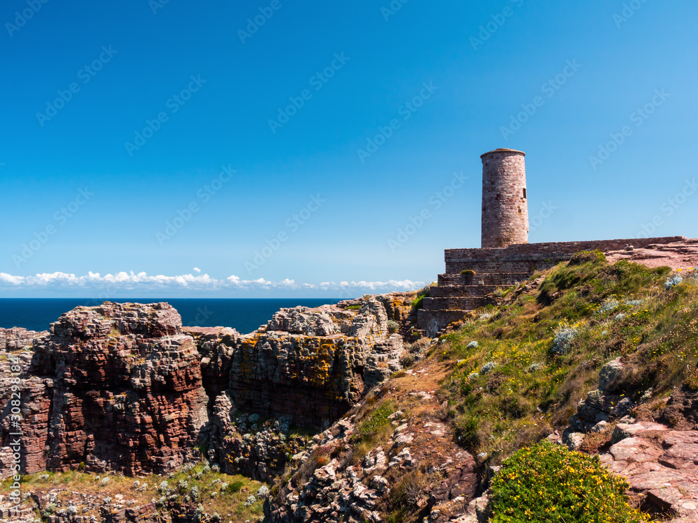 A scenic view of the cliffs on a coast of the Atlantic ocean with a lighthouse in background.