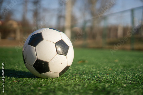 A black and white soccer ball on an artificial turf on a clear sunny day.