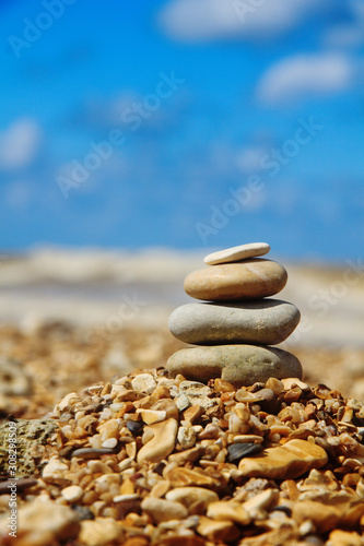 Stone pyramid on shore on blurred blue background. Balance symbol. Vertical backdrop with copy space