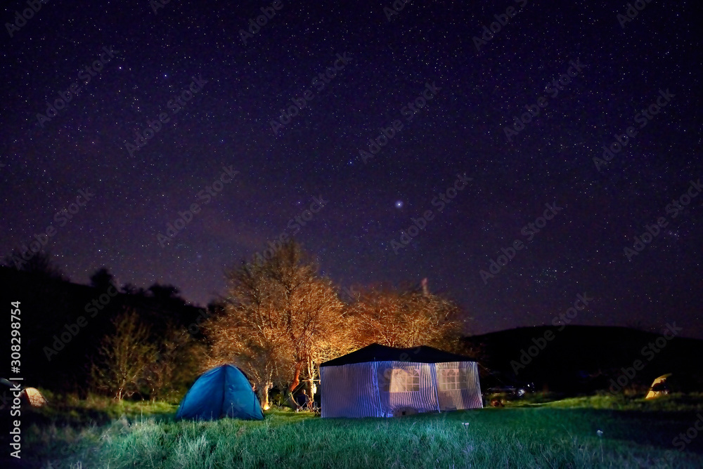 Illuminated yellow camping tent under stars at night