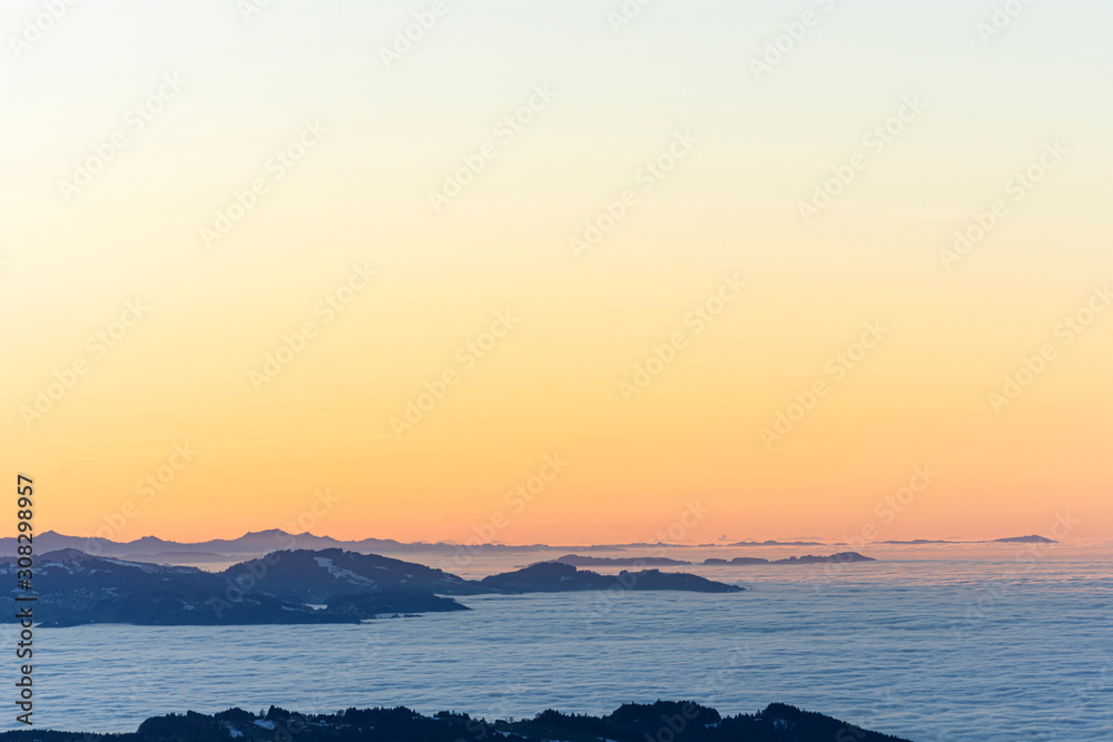 Colorful sunset at the edge of the Alps with snow-covered, forested hills. Fog over the Rhine valley and the lowlands. Austria, Switzerland. Lots of copy space