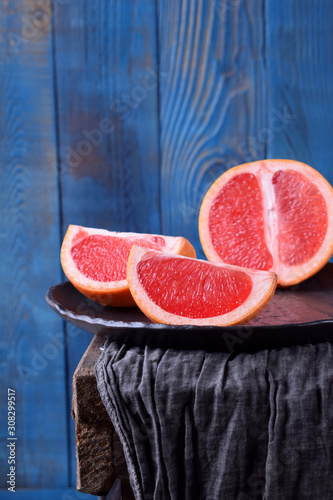 Slices of red grapefruit on the black plate against the blue wooden background