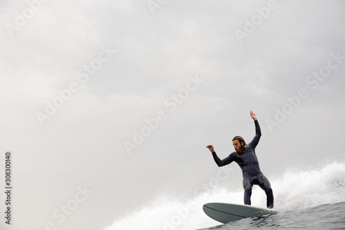 Canvas Print Man in the black diving suit with a beard riding on the surf hands up