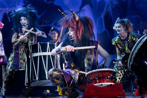 Traditional Japanese performance. Taiko drummers in a wigs and a demon masks perform on stage with drum on a dark background. Demons from Japanese mythology.
