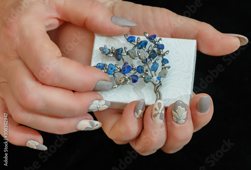 Fotografering Female hands with a multicolored manicure and a brooch with blue stones closeup
