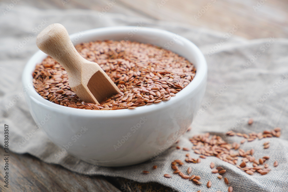 White bowl of whole flax seeds, linseeds on wooden table.le. White bowl of whole flax seeds, linseeds on wooden table.le.