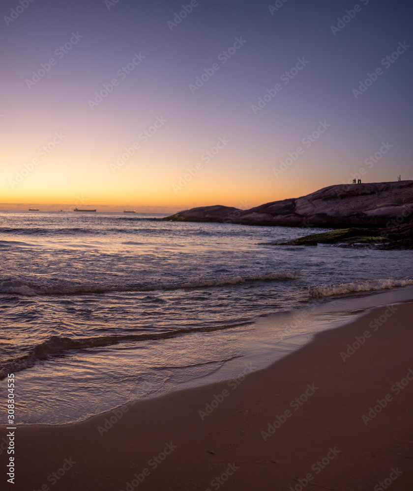 Purple orange glow glow at daybreak at the Arpoador Devil's beach in Rio de Janeiro with waves coming in reflecting first light with pristine beach Purple orange glow glow at daybreak at the Arpoador Devil's beach in Rio de Janeiro with waves coming in reflecting first light with pristine beach