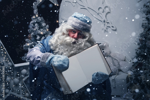 Russian Santa Claus (Grandfather Frost) in a blue caftan sits and holds in his hands a large open book with empty pages for wishes. Classic blue color 2020