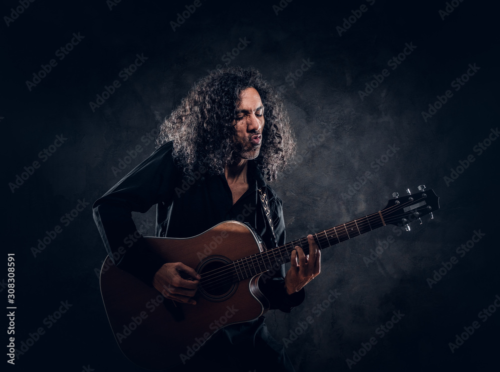 Curly man with guitar is presenting his new acoustic masterpiece at studio.