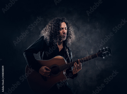 Curly man with guitar is presenting his new acoustic masterpiece at studio.