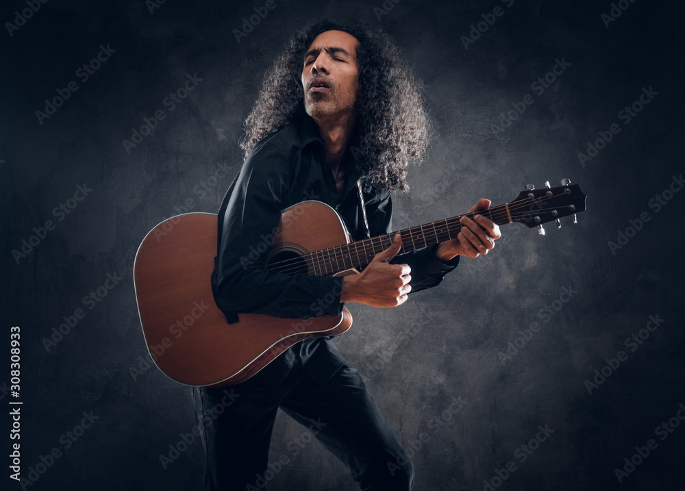 Fototapeta premium Middle aged emotional singer is playing an acoustic guitar at dark studio.