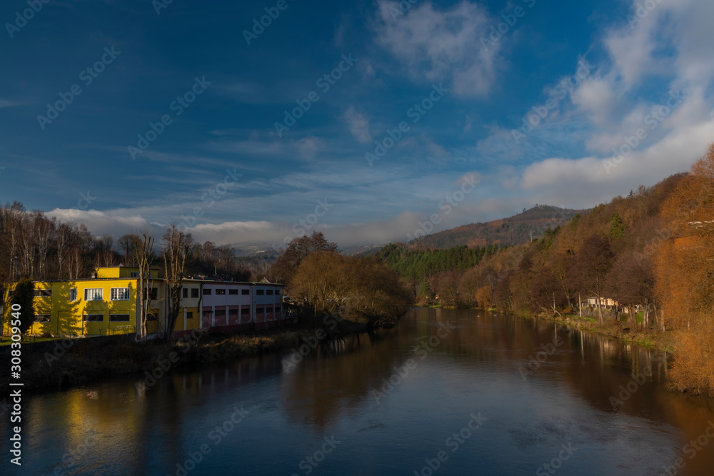Ohre river in Perstejn village with blue sky and color forests and mountains