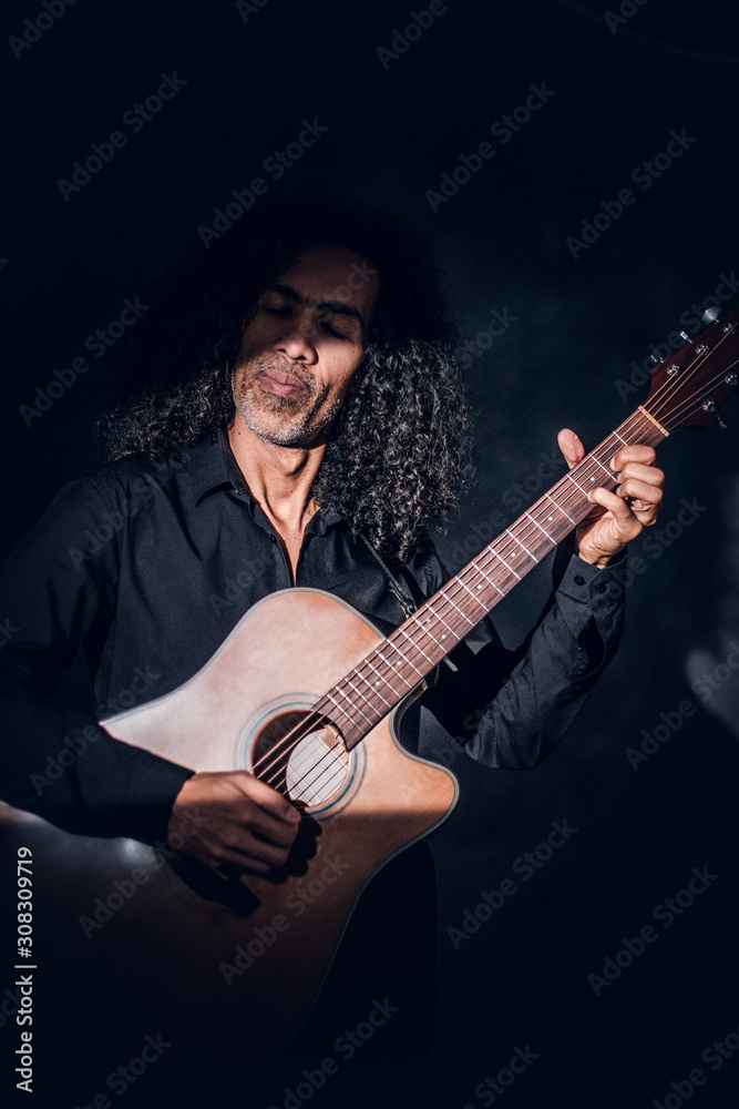 Obraz premium In dark photo studio curly middle aged man is posing with guitar for photographer.