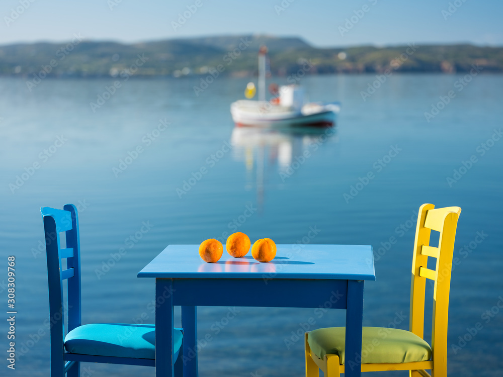 three orange oranges on the blue table with seats and sea view in Greece