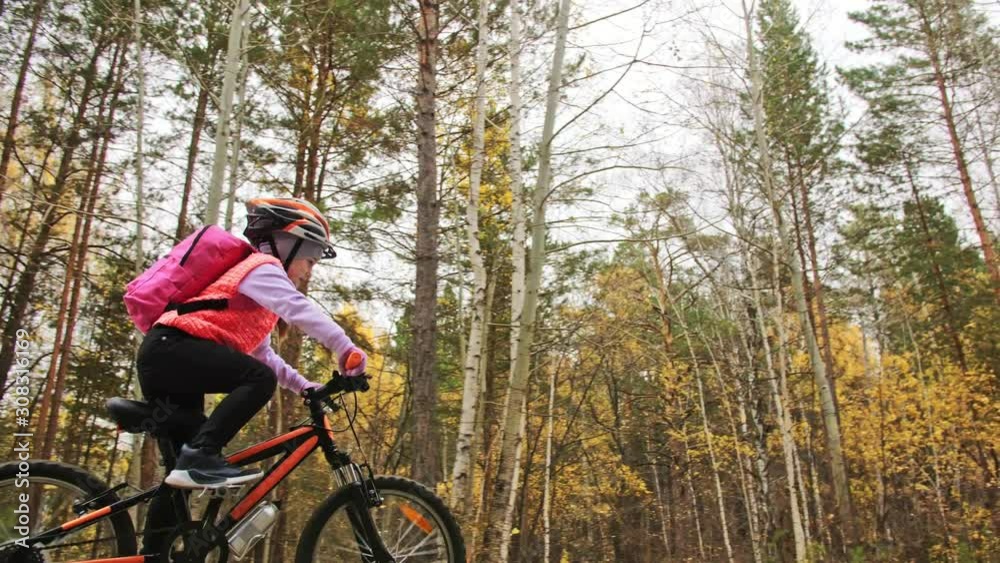 One caucasian children rides bike road in autumn park. Little girl riding black orange cycle in forest. Kid goes do bicycle sports. Biker motion ride with backpack and helmet. Mountain bike hardtail. One caucasian children rides bike road in autumn park. Little girl riding black orange cycle in forest. Kid goes do bicycle sports. Biker motion ride with backpack and helmet. Mountain bike hardtail.