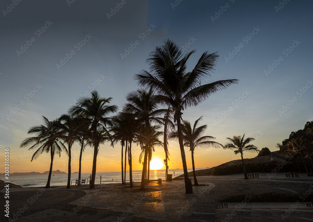 Sunrise on the Arpoador boulevard with the Devils beach and silhouetted palm trees in Rio de Janeiro against a clear sky 