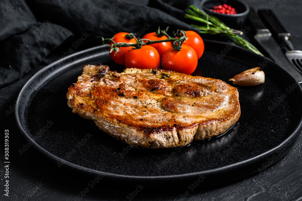 Roast pork steak with tomatoes. Black background. Top view