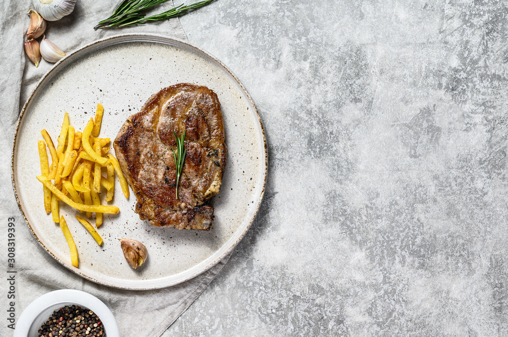 Grilled pork steak on bone with French fries. Gray background. Top view. Space for text