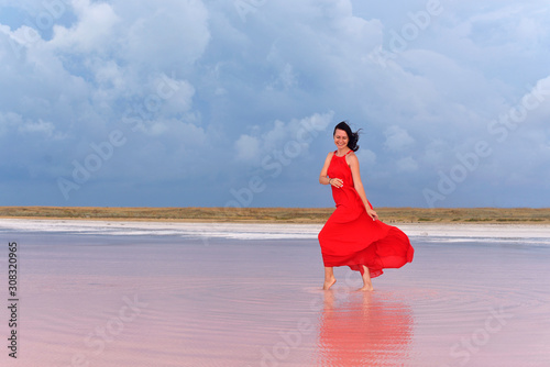 A young woman in a long red dress walks on the lake before the coming storm