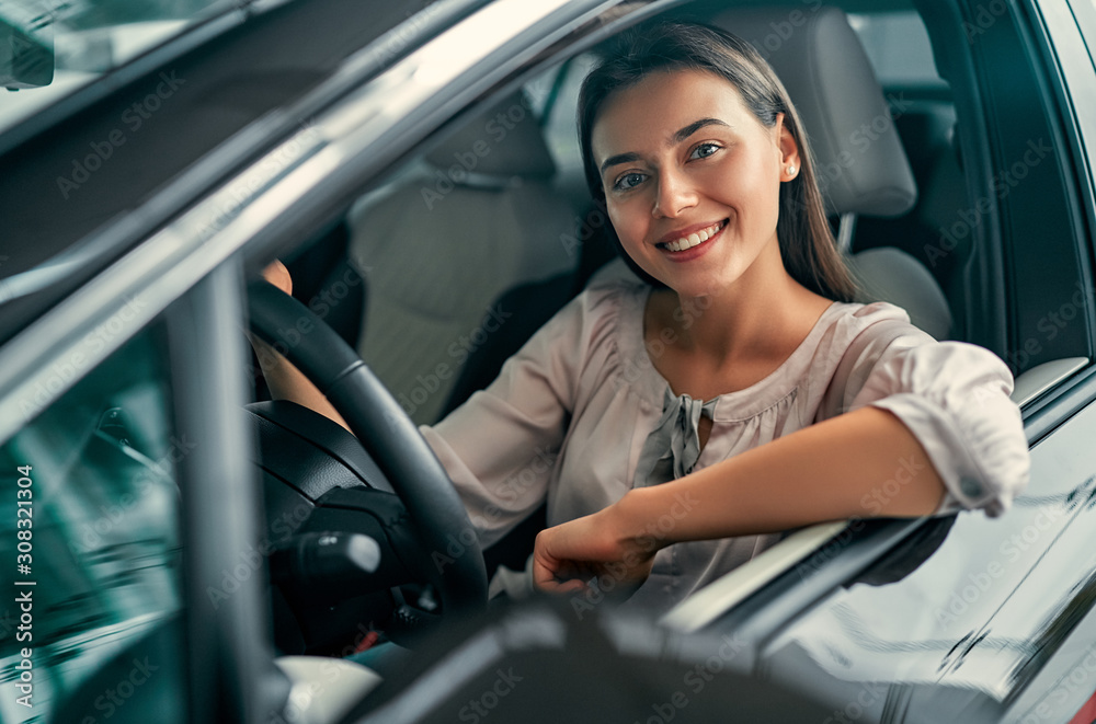 Young beautiful woman is choosing a new vehicle in car dealership. Lady in a car salon. Woman buying the car. Young beautiful woman is choosing a new vehicle in car dealership. Lady in a car salon. Woman buying the car.