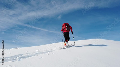 Ski Mountaineer climbs a snowy mountain over blue clear sky. Winter season, sunny day. Concepts: achieve a personal goal, exploration, new horizons.