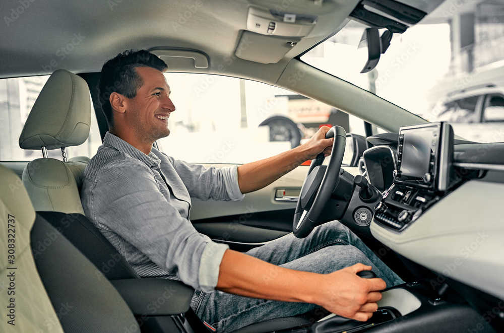 Young man is sitting in car and choosing a new vehicle in car dealership. Young man is sitting in car and choosing a new vehicle in car dealership.
