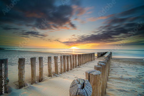 Fototapeta Naklejka Na Ścianę i Meble -  Groynes and wave breakers in a smooth sea just before sunset at a Dutch coast